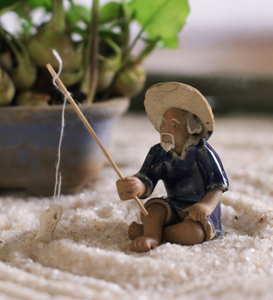 Old Fisherman In Blue On Ground With Fishing Rod